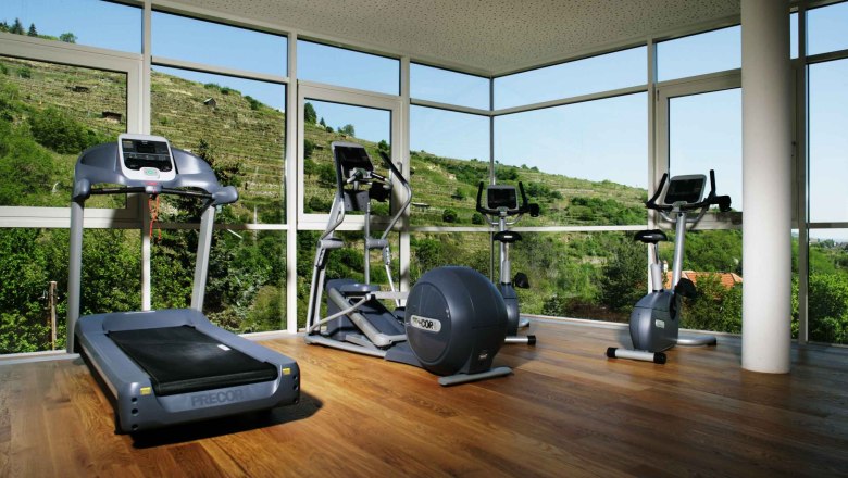 Fitnessraum, © Steigenberger Hotel and Spa, Andreas Hofer Fitnessraum mit Laufband, Crosstrainer und Heimtrainer vor großen Fenstern mit Blick auf grüne Hügel.