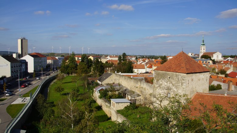 Stadtgraben Bruck an der Leitha, © Erwin Huber Stadtansicht von Bruck an der Leitha mit Stadtmauer, Kirche und Windrädern im Hintergrund.
