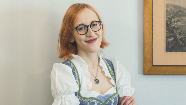 Im Service: Magdalena Bauer, © Niederösterreich Werbung/David Schreiber Eine Frau mit Brille und Dirndl lächelt vor einem Bild an der Wand.