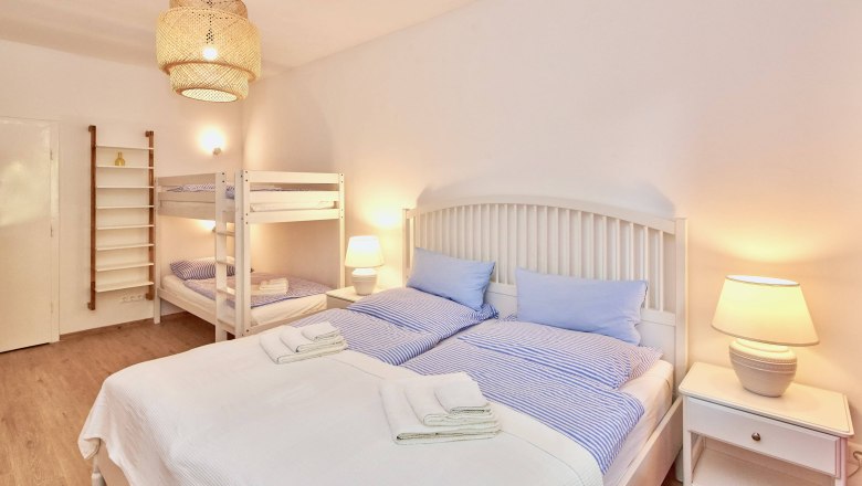 Top 1 - Schlafzimmer, © VP FeWo OG Schlafzimmer mit Doppelbett, Etagenbett, Nachttischlampen und heller Einrichtung.