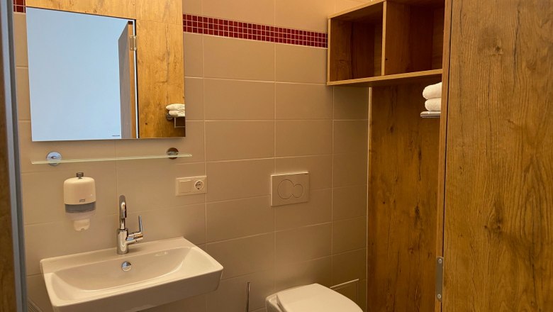 Badezimmer mit Dusche und WC, © Wiener Alpen Modernes Badezimmer mit Waschbecken, Spiegel, WC und Holzregal.