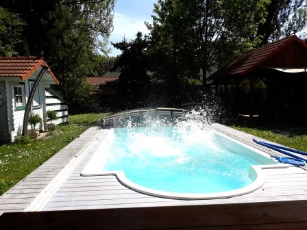 Pool, © bed and pool Ein Pool im Garten mit spritzendem Wasser, umgeben von Bäumen und einem kleinen Gebäude mit rotem Dach.