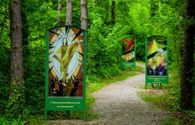 Gläserner Kreuzweg Bad Erlach, © Marktgemeinde Bad Erlach, Harald Wrede Weg durch einen Wald, links und rechts neben dem Weg stehen große Tafeln aus Glas, die die Stationen des Kreuzweges darstellen.