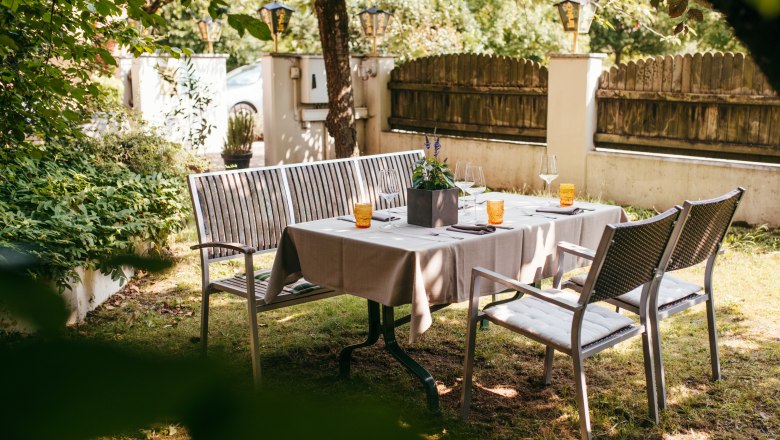 Idyllisch speisen unterm Dirndlstrauch, © Niederösterreich Werbung/Daniela Führer Gedeckter Tisch im Garten mit Stühlen und Bänken unter Bäumen.
