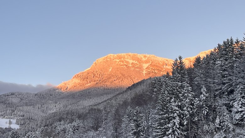 Aussicht Winter RaxChalet, © RaxChalet Verschneite Berglandschaft mit orange beleuchtetem Gipfel im Sonnenuntergang.