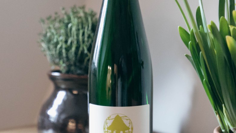 Wein aus eigener Erzeugung, © Monika Pölzer Eine Flasche Grüner Veltliner Wein steht auf einem Tisch neben gelben Blumen und einem Topf mit Kräutern.