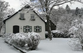 Landsitz Oberhof, © Landsitz Oberhof Verschneites Haus mit grünen Fensterläden und Bäumen im Hintergrund.