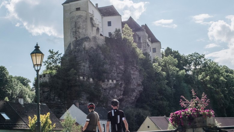 Burg Raabs, © Niederösterreich Werbung, Jiri Dužár Zwei Radfahrer stehen auf einer Brücke mit Blick auf die Burg Raabs, die auf einem Felsen thront.