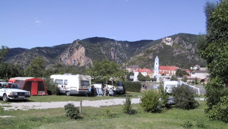 Campingplatz Rossatzbach, © Campingplatz Rossatzbach Campingplatz mit Wohnwagen und Zelten vor einer Berglandschaft und einer Kirche im Hintergrund.