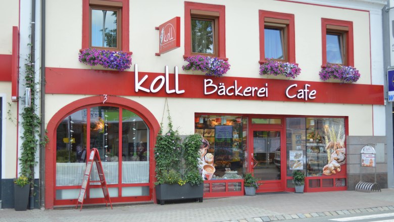 Koll Bäckerei Café in Kirchschlag, © Koll GmbH Außenansicht der Koll Bäckerei Café in Kirchschlag mit roten Fensterrahmen und Blumenkästen.