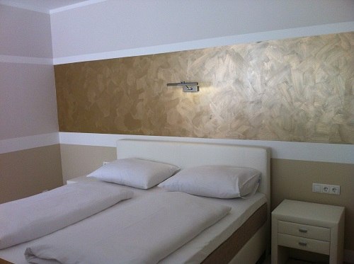 Zimmer, © Kurtschack KG Modernes Schlafzimmer mit Doppelbett und goldener Wanddekoration.