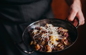 Blunzengröstl mit Sauerkraut, © Niederösterreich Werbung/Daniela Führer Eine Person hält eine Pfanne mit Blunzengröstl, garniert mit geriebenem Käse.