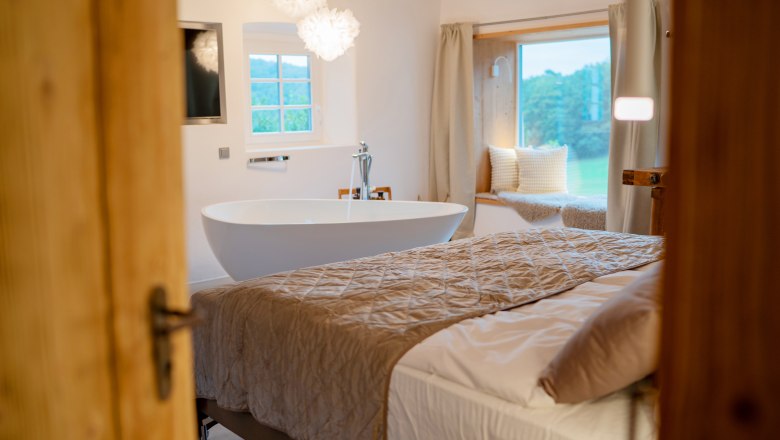 Chalet´s & Plätze voller WUNDER - Weidehaus De Luxe, © WUNDERVOLL eben Innenansicht eines luxuriösen Schlafzimmers mit freistehender Badewanne, großem Bett und Fensterplatz mit Kissen.