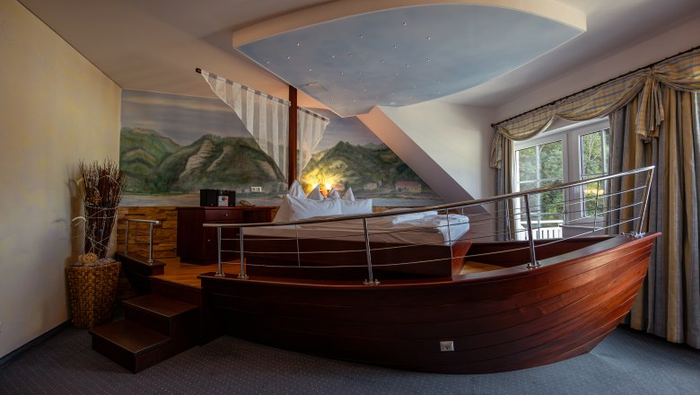 Hotel ResidenzWachau, © Niederösterreich Werbung / Maximilian Pawlikowsky Hotelzimmer mit Bett in Form eines Bootes, Wandgemälde von Landschaft, Fenster mit Vorhängen.