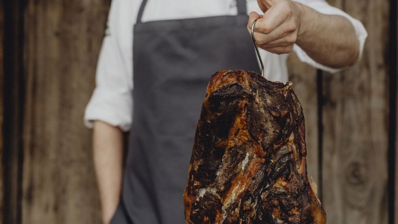 Selbstgeräucherter Emmerberger Rauchschinken, © Niederösterreich Werbung/Sophie Menegaldo Person hält geräucherten Schinken an einem Haken.