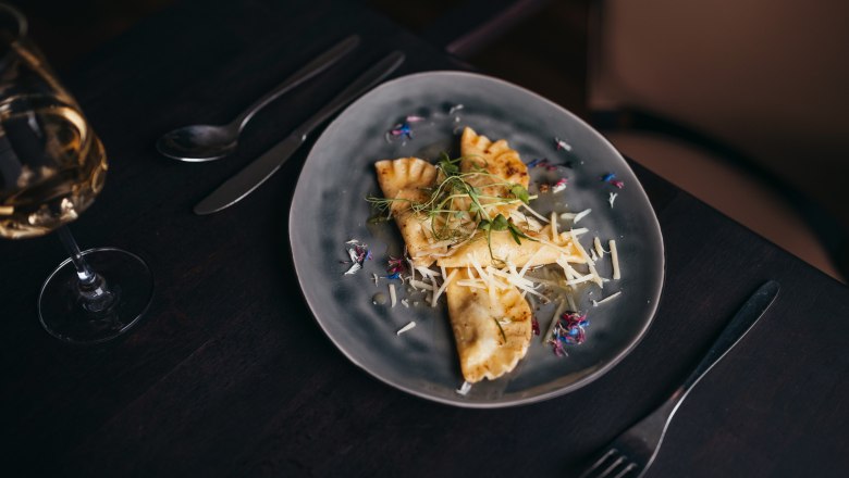 Ganslravioli in Rosmarinbutter, © Niederösterreich Werbung/Daniela Führer Gedeckter Tisch mit gefüllten Teigtaschen und geriebenem Käse auf grauem Teller.