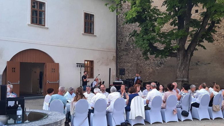 Tafeln im Weinviertel, © Weinviertel Tourismus GmbH Menschen sitzen an einem langen Tisch im Freien, umgeben von alten Gebäuden und einem Baum.