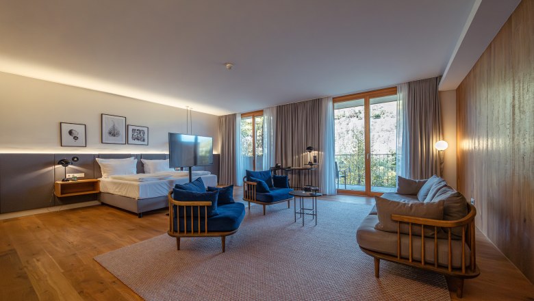 Steigenberger Hotel & Spa, Krems, © Niederösterreich Werbung/ Maximilian Pawlikowsky Modernes Hotelzimmer mit Holzboden, großem Bett, blauen Sesseln und großen Fenstern mit Vorhängen.
