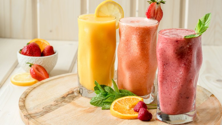 Smoothies, © Koll GmbH Drei Smoothies in Gläsern auf einem Holzbrett, dekoriert mit Obst und Minze.