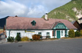 Schneebergmuseum Puchberg, © Schneebergmuseum Schneebergmuseum Puchberg, ein traditionelles Gebäude mit grünem Dach und Schornstein, umgeben von Bergen und Bäumen.