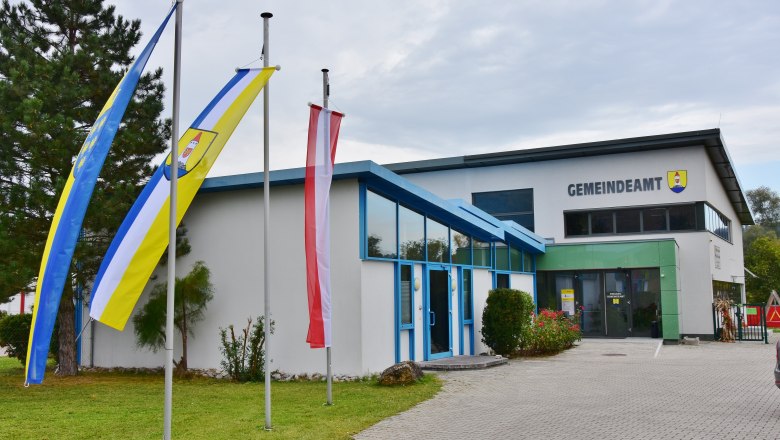 Gemeindeamt, © Gemeinde Seebenstein Ein modernes Gebäude mit der Aufschrift 'Gemeindeamt' und drei Fahnenmasten davor.