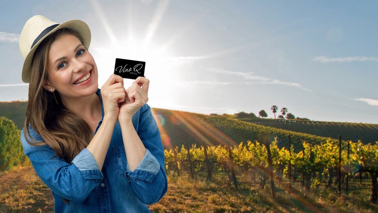 VinoQ, © ohida OG / ohne.media Frau mit Hut hält VinoQ-Karte vor einem sonnigen Weinberg.