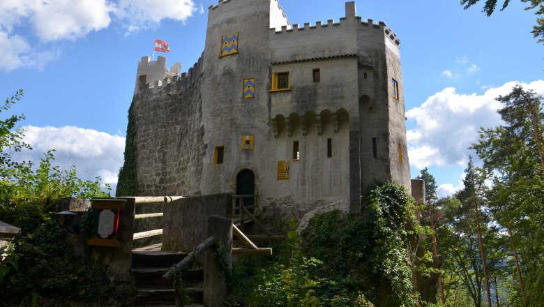 Burg Grimmenstein, © Marktgemeinde Grimmenstein Burg Grimmenstein mit Brücke, Zinnen und blau-gelb gestrichenen Fensterläden im Grünen.