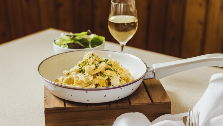 Beliebter Klassiker: Eiernockerl, © Niederösterreich Werbung/David Schreiber Eiernockerl in einer Pfanne mit einem Glas Weißwein und einem Salat im Hintergrund.