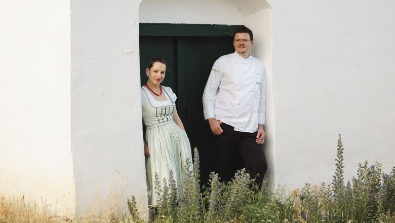 Wirtsleute Daniela und Harald Graf, © Niederösterreich Werbung/Michael Reidinger Zwei Personen stehen in einem Türrahmen vor einem weißen Gebäude.