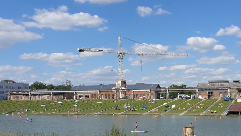 korneuburg-donau-werftbad-liegewiese, © SEFKO Menschen entspannen auf einer Liegewiese an einem Fluss mit einem Kran im Hintergrund.
