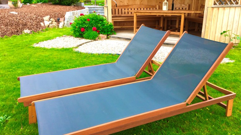 Garten, © Foto: Eva Zwirner Zwei blaue Liegestühle auf grünem Rasen vor einer Holzhütte im Garten.