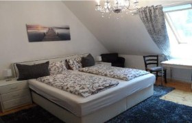 Doppelzimmer Ried Goissenberg, © Familie Denk Gemütliches Doppelzimmer mit Bett, Nachttischen, Tisch und Stühlen, dekoriert mit einem Bild und einem Kronleuchter.