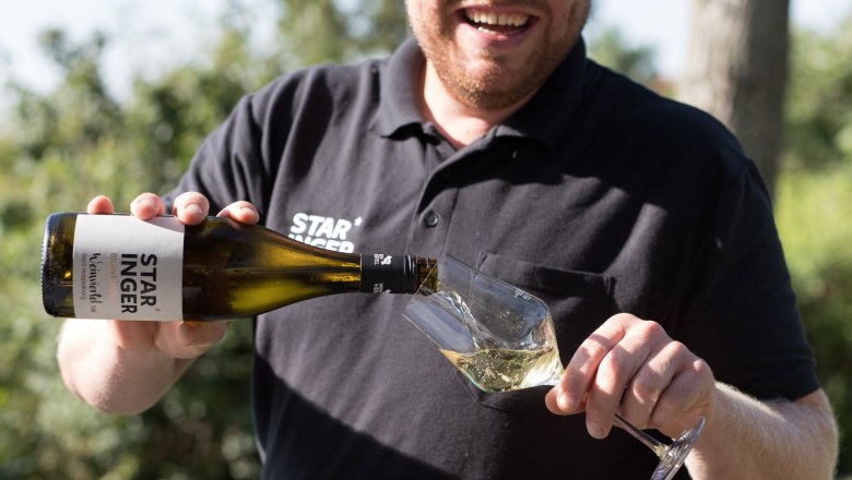 Weingut Staringer, © Anita Thiebet Mann schenkt Wein in ein Glas im Freien ein.