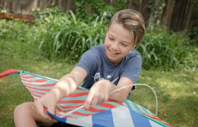 Kind beim Spielen, © Weinviertel Tourismus GmbH / Lahofer Ein Kind sitzt im Gras und hält einen bunten Drachen.