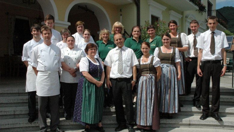 Team, © Reiböck Gruppe von Menschen in traditioneller und beruflicher Kleidung vor einem Gebäude.