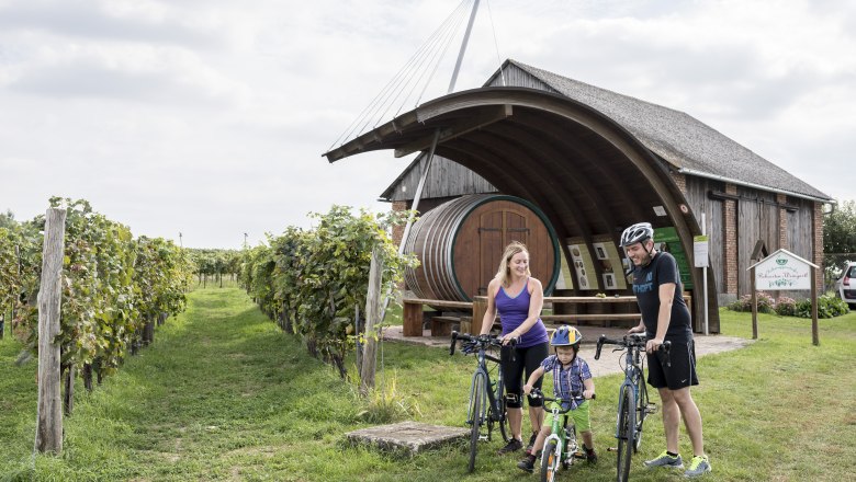 Erlebnisweingartl Hohenruppersdprf, © Weinviertel Tourismus GmbH / Herbst Eine Familie mit Fahrrädern vor einem Weingut mit großem Fass in Hohenruppersdorf.