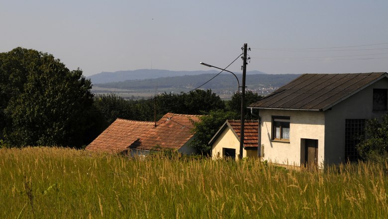 Kellergasse Putzing, © Weinviertel Tourismus / Mandl Ländliche Szene mit Häusern und Wiesen im Vordergrund, Hügel im Hintergrund.