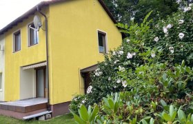 Garten im Ferienhaus am Schloßpark, © Wiener Alpen Gelbes Haus mit Terrasse und blühenden Sträuchern im Vordergrund.