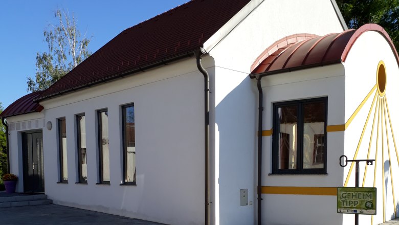 Amethystkapelle Grübern, © Stadtgemeinde Maissau Weiße Kapelle mit rotem Dach und gelben Akzenten, umgeben von gepflastertem Boden und Pflanzen.
