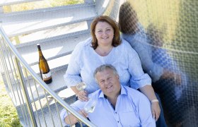 Regina & Martin Weineck, © Michael Himml Ein Mann und eine Frau sitzen auf einer Metalltreppe mit Weingläsern in der Hand.