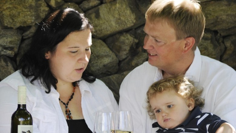 Familie, © Steve Haider Eine Familie sitzt an einem Tisch mit zwei Weingläsern und einer Weinflasche vor einer Steinmauer.