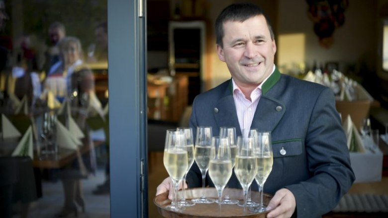 Czipin Leonhard serviert, © Robert Herbst Ein Mann in traditioneller Kleidung serviert Sektgläser auf einem Tablett.