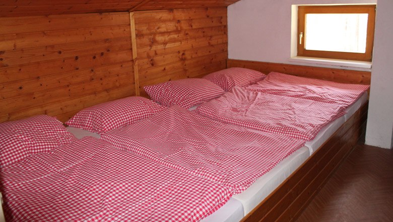 Schlafen im Himbergerhaus, © Naturfreunde Himberg, Johann Bernsteiner Drei Betten mit rot-weiß karierten Bettbezügen in einem holzverkleideten Raum.