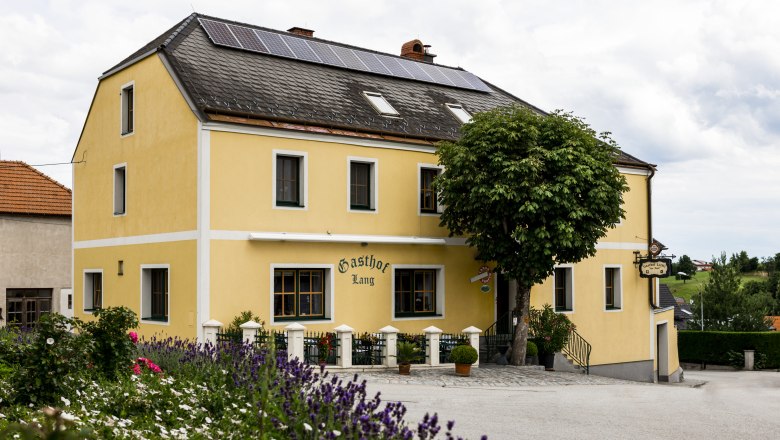 Wirtshaus in Weinzierl am Walde, © Niederösterreich Werbung/David Schreiber Gelbes Gasthaus mit Solarpanelen auf dem Dach, umgeben von Blumen und Bäumen.