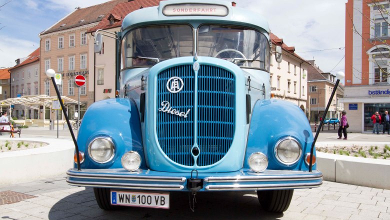 Oldtimer Bus aus 1961, © Michael Weller Ein blauer Oldtimer-Bus aus dem Jahr 1961 steht auf einem Platz vor Gebäuden.