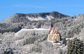Wolfgangskirche, © Marktgemeinde Kirchberg a.W./Wolfgang Riegler Winterlandschaft mit Kirche vor bewaldetem Hügel.