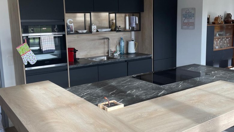 Küche, © Regina Schimmer Moderne Küche mit Holz- und Marmorelementen, drei Hängelampen und schwarzen Schränken.