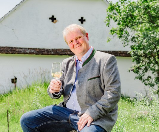 Weingut Hofbauer, © Leonardo Ramirez Mann sitzt auf einem Stein im Grünen und hält ein Weinglas in der Hand.