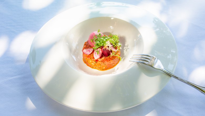 Kulinarik im Hotel Richard Löwenherz, © Chris Saupper Ein kunstvoll angerichtetes Gericht auf einem weißen Teller mit einer Gabel daneben.