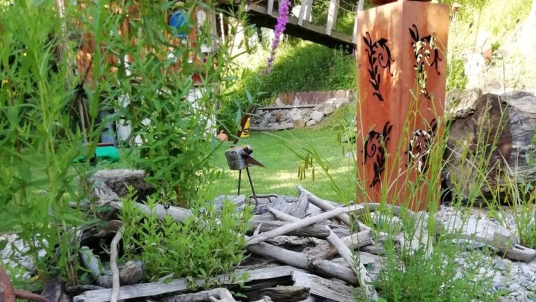 img_1034_ausschn_c_tina-perina, © Tina Perina Garten mit Holzskulptur, Pflanzen und dekorativen Elementen.